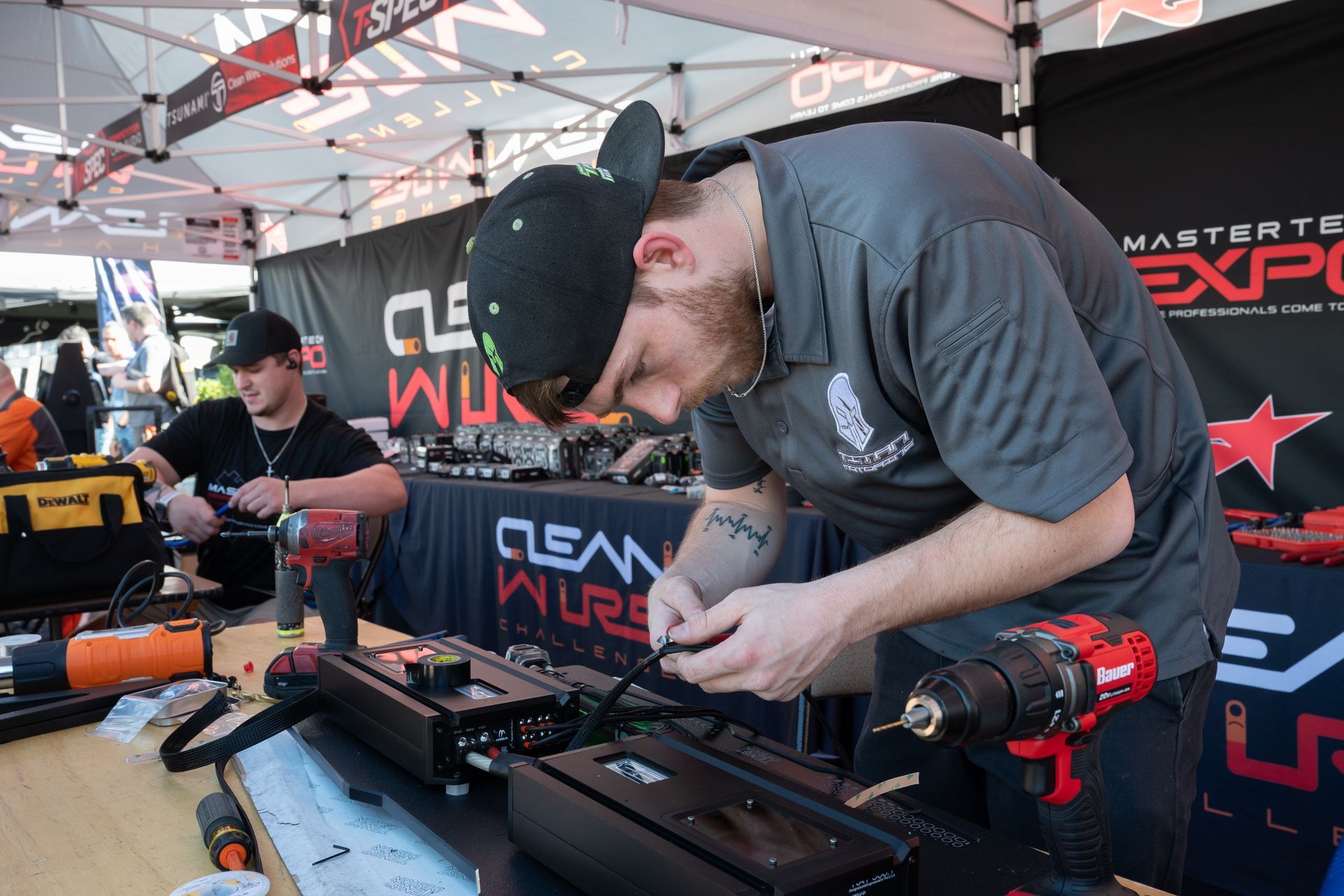Two men assembling electronics at an outdoor event. One man using a drill, the other works with wires.