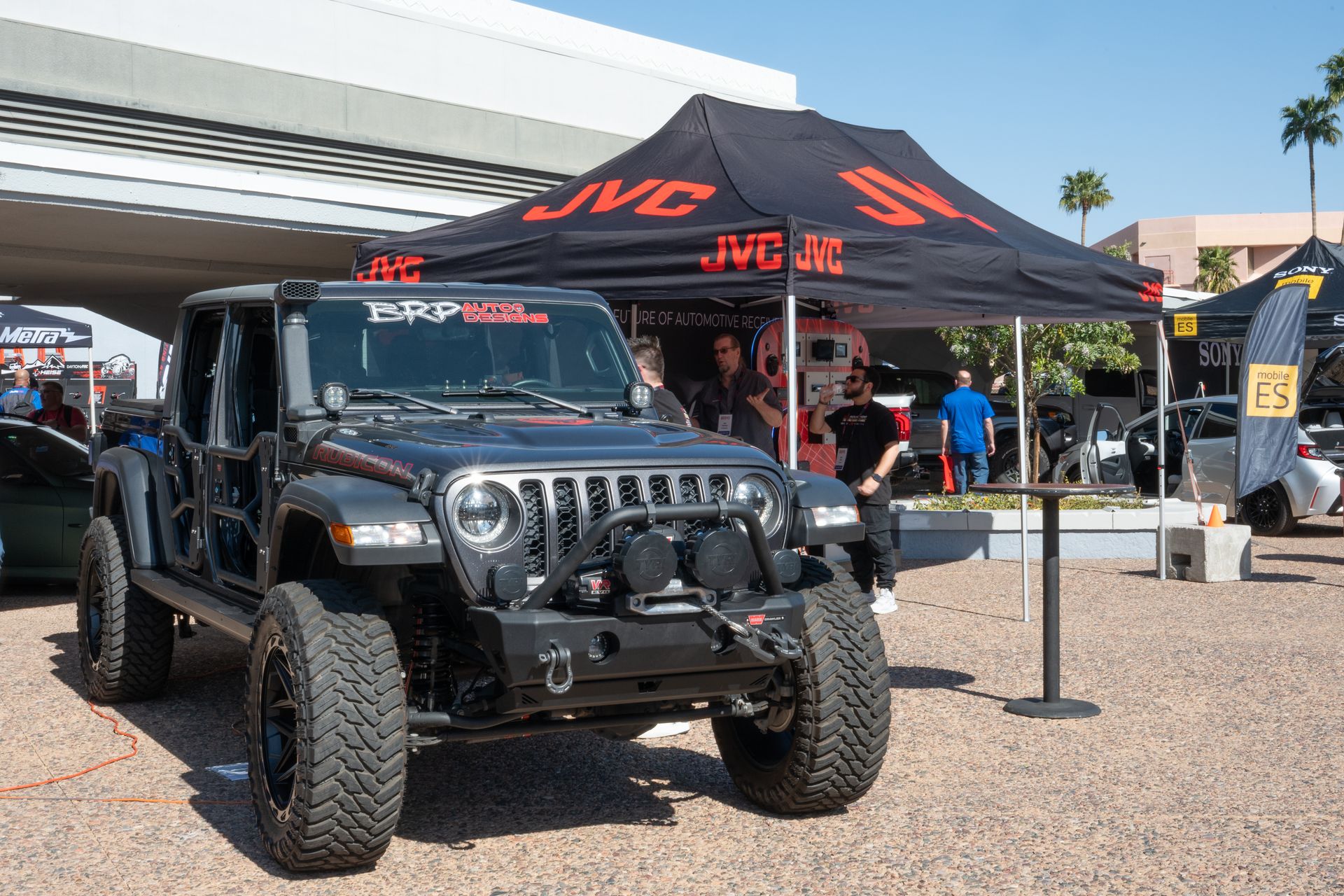 Black Jeep Wrangler with modifications parked under a JVC tent at an outdoor event.