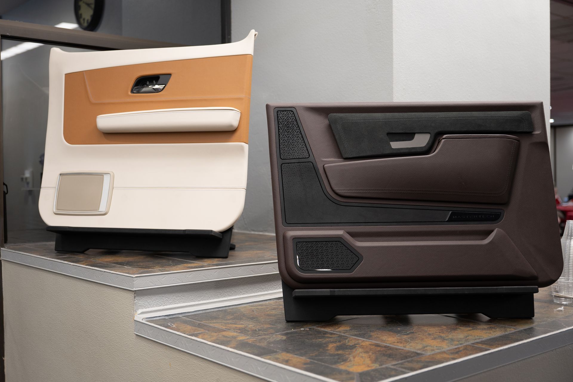 Two car door panels: white and tan, brown and black. Displayed on a shelf with speakers and handles.