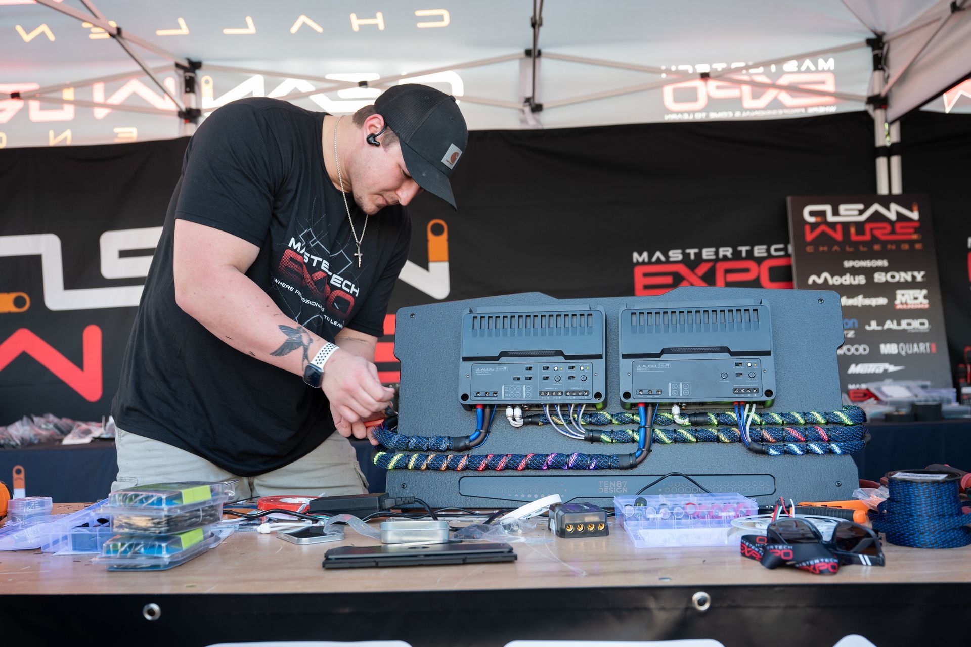 Man in a cap working on electronic components at an expo table; black, gray, and colorful wires.