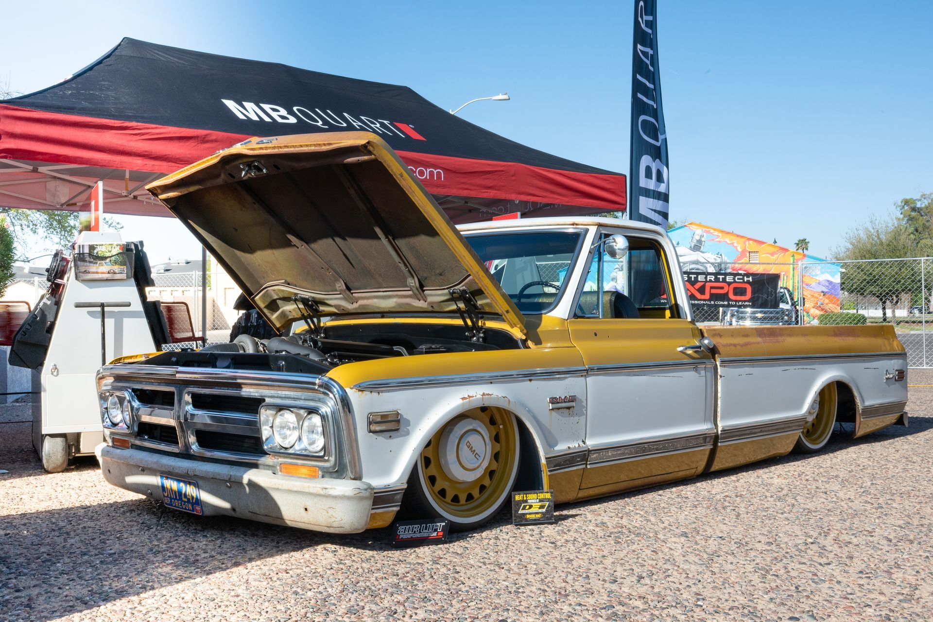 Custom yellow and white pickup truck with hood open on display at a car show.