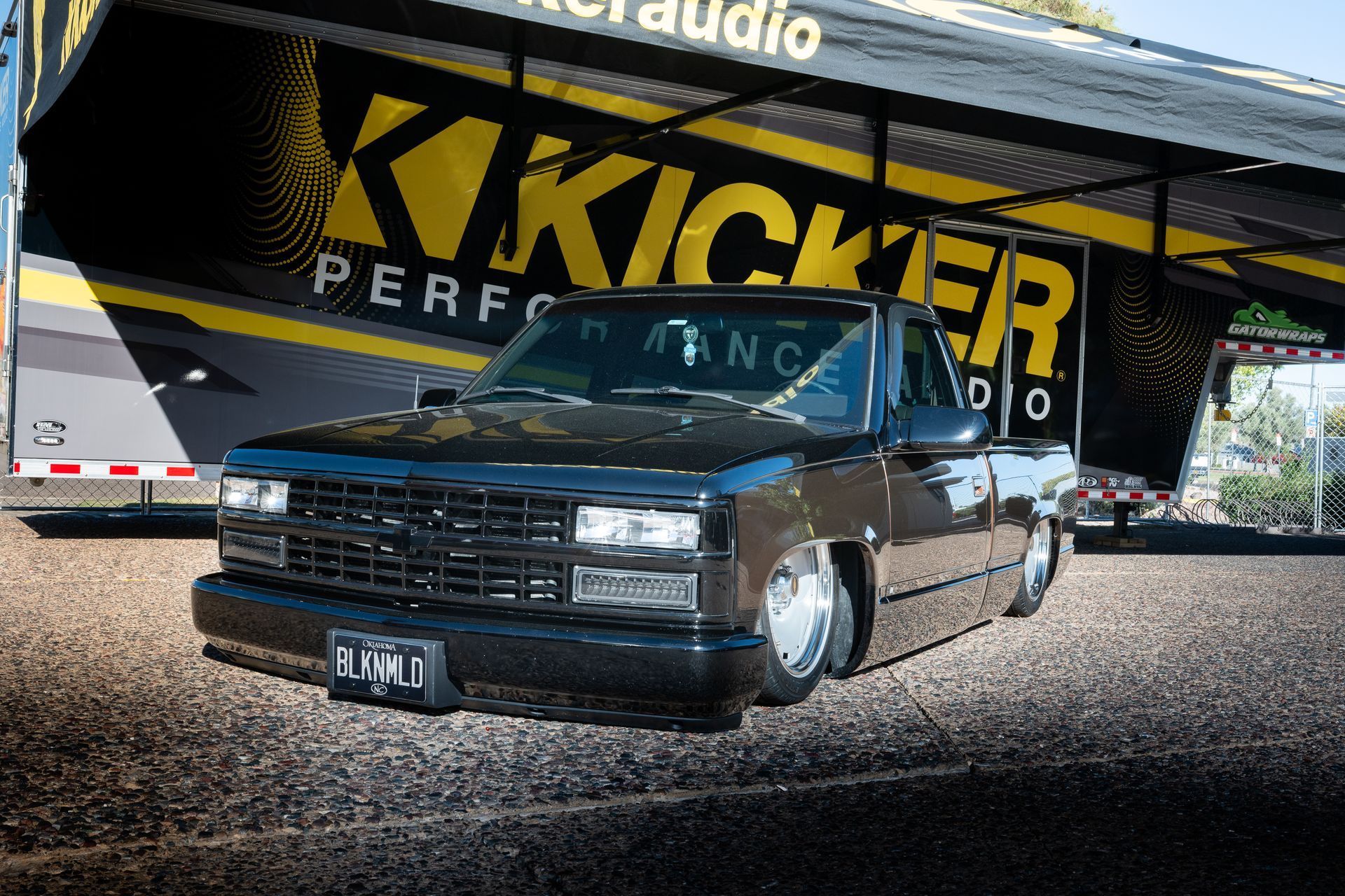 Black lowered Chevy pickup truck parked in front of a Kicker audio trailer.