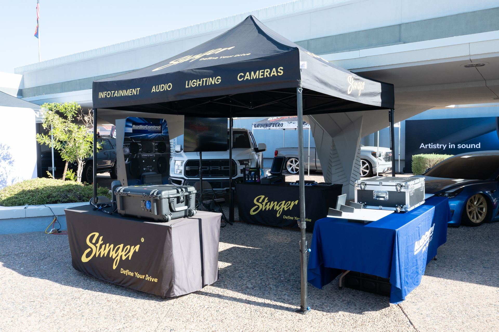 Stinger booth at an outdoor event with tables, canopy, and equipment. Tables have black and blue covers with the company logo.