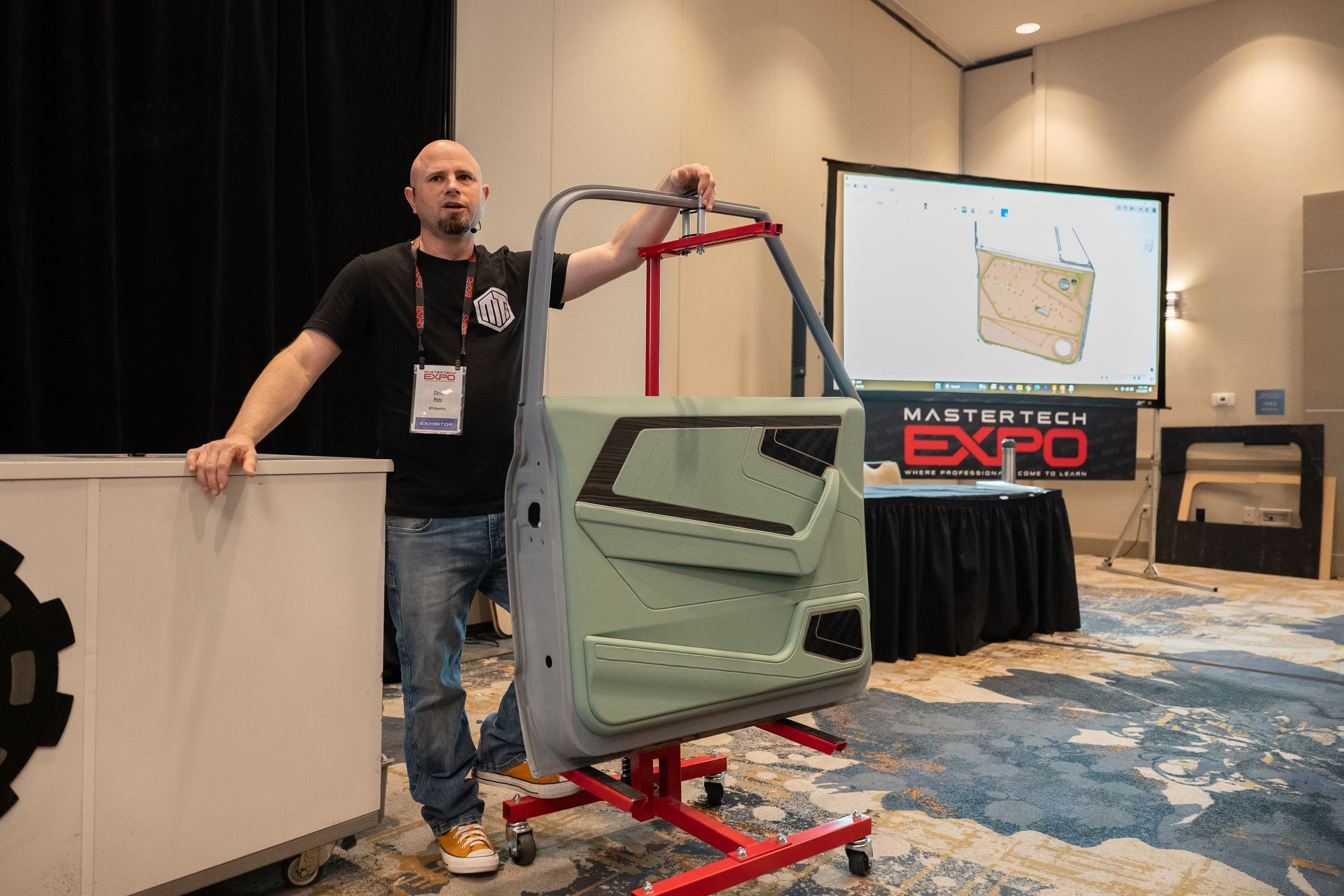 Man holds car door at a conference. Presentation screen and 