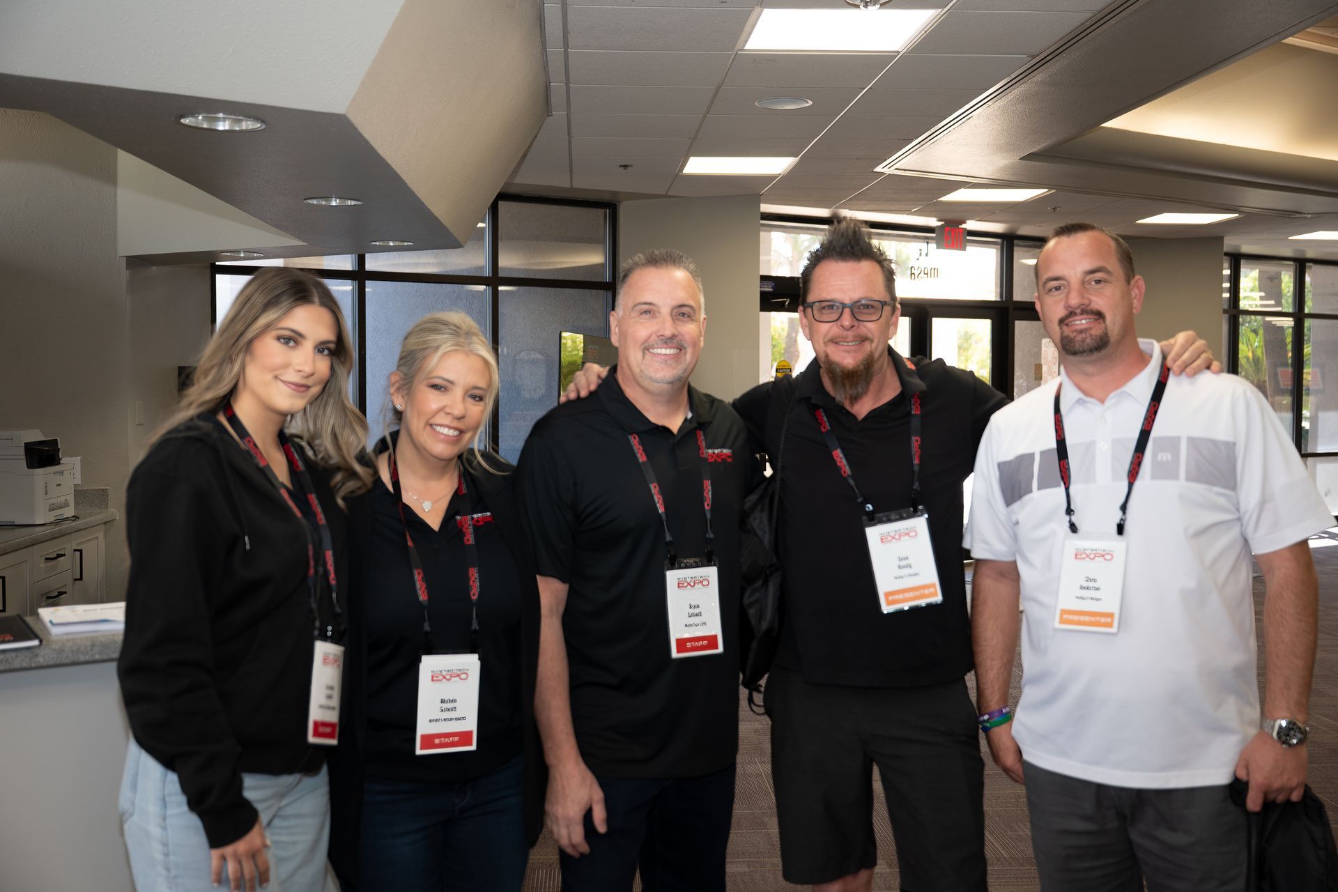 Five people in a hallway wearing lanyards, smiling at the camera.