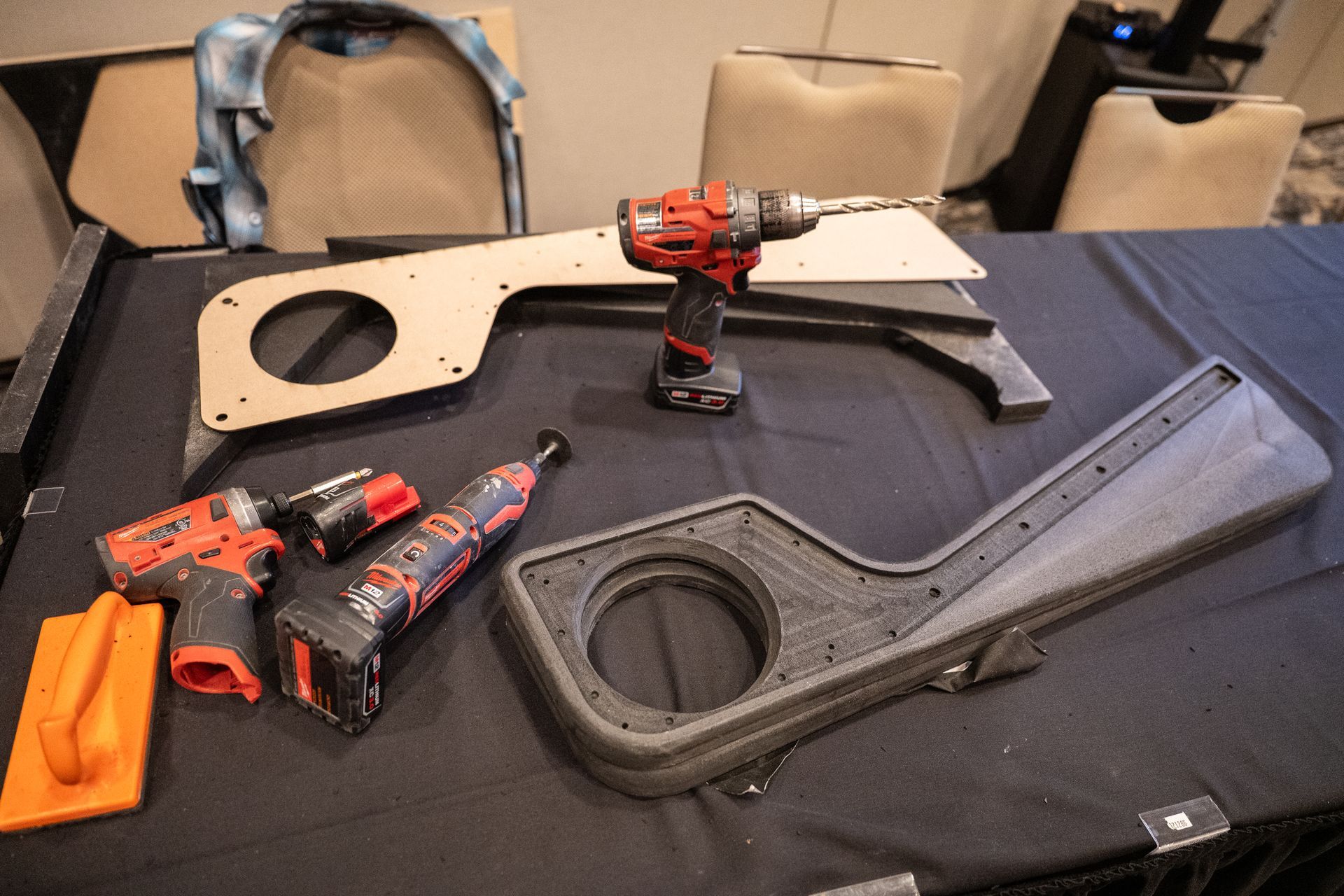 Tools and parts laid out on a table: drills, a sanding block, and beige and black mounting pieces.