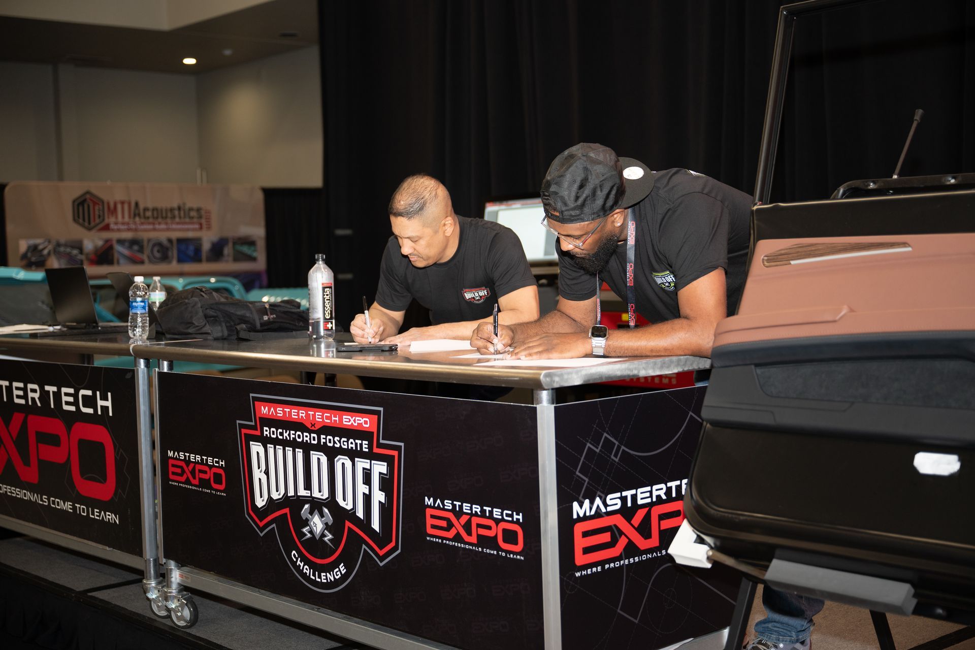 Two men at a booth, signing papers. 