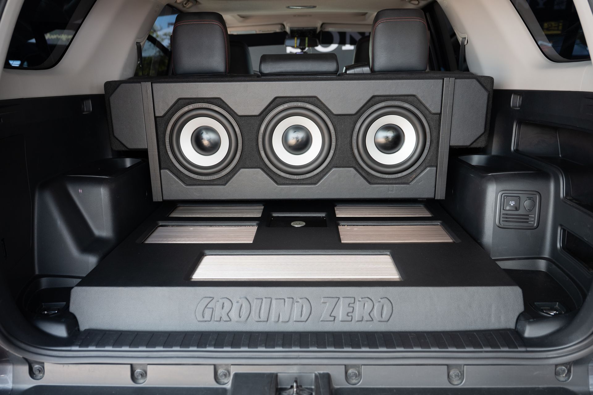 Vehicle's open trunk interior with a custom subwoofer enclosure and amplifiers by Ground Zero.