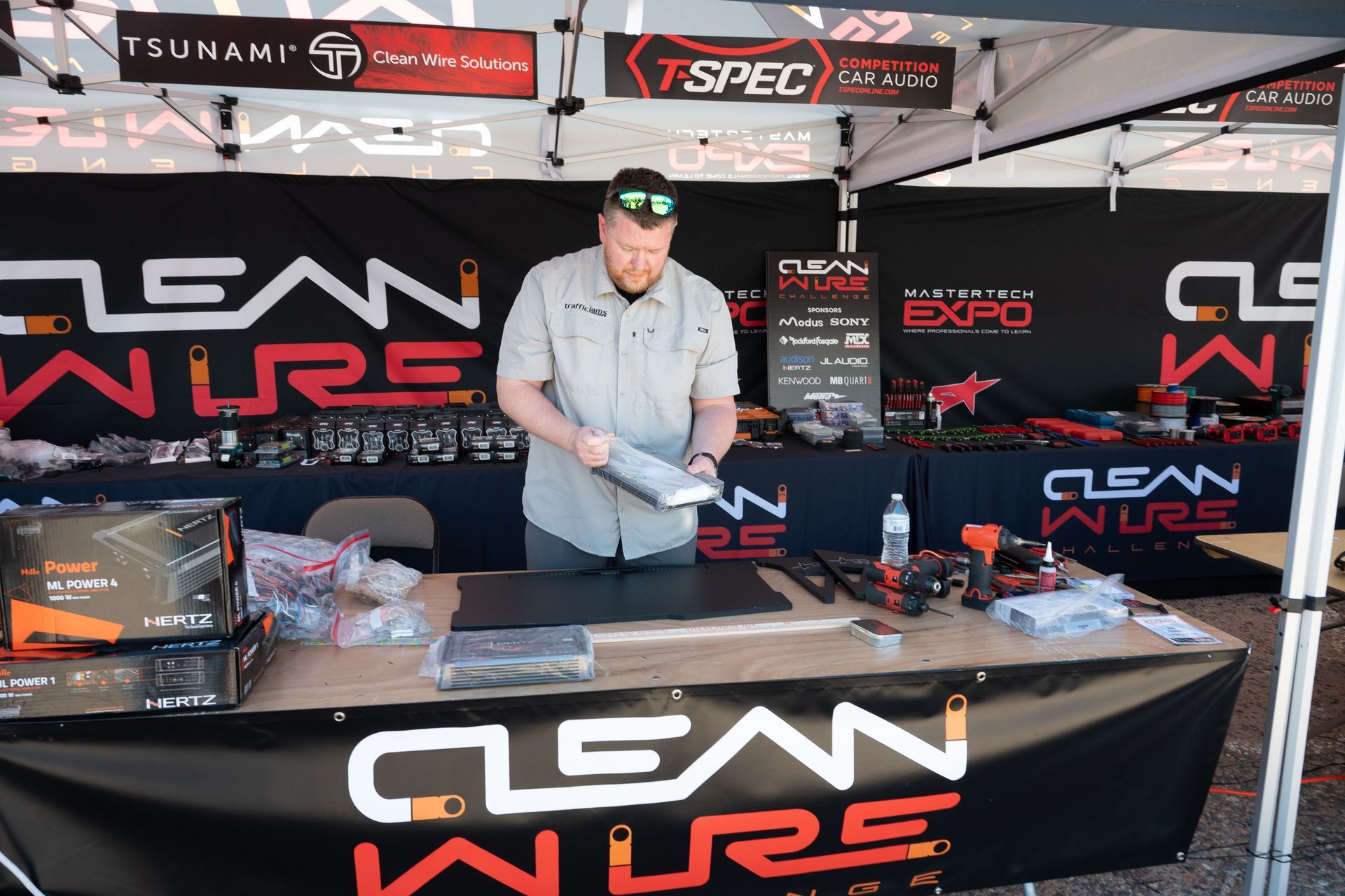 Man at Clean Wire Expo booth, demonstrating product. Black table with tools, products, backdrop with logo.