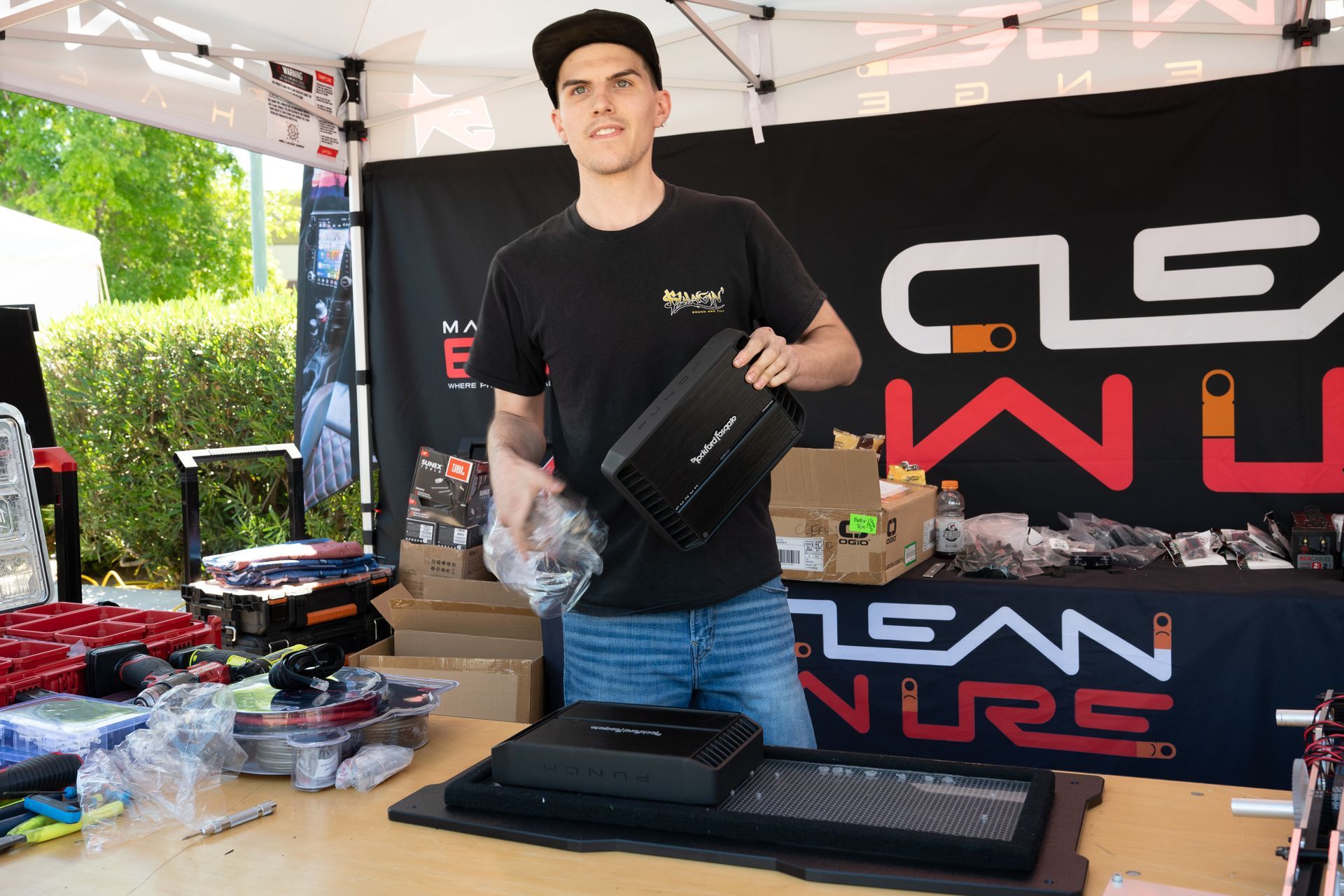 Man at a vendor table holds a black product, smiling. Table has products & Clean Culture logo.