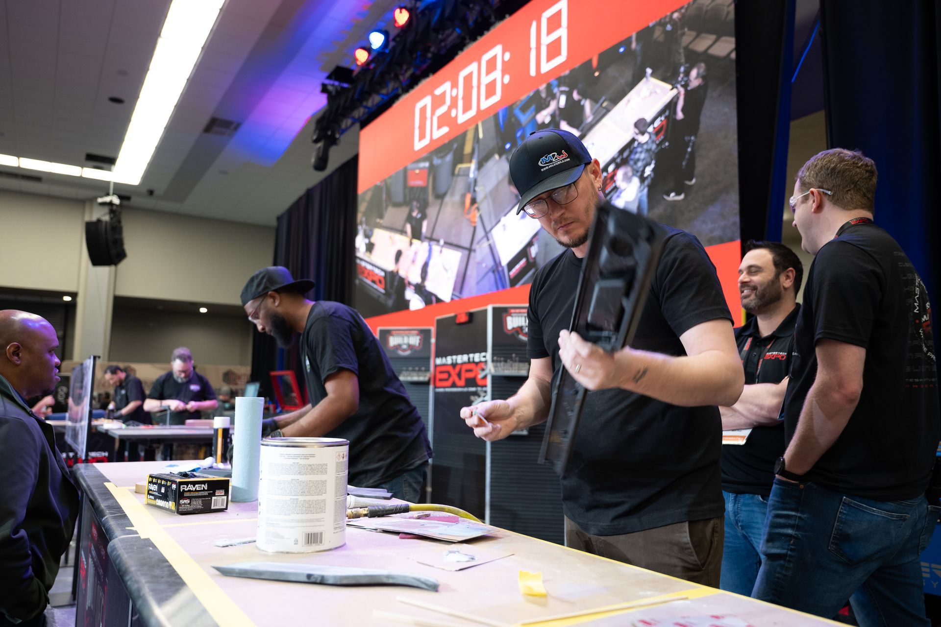 People working at a table, possibly in a competition. A timer displays 02:08:18.