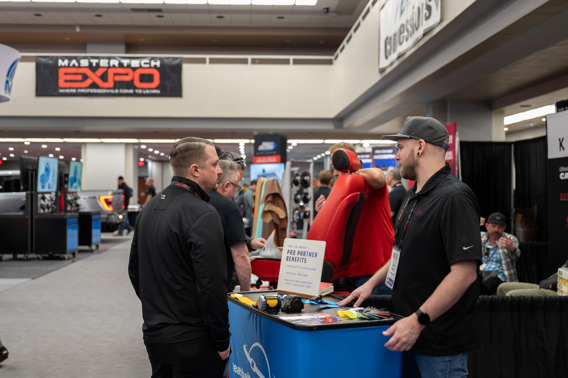People at a trade show booth, looking at items on a table. 