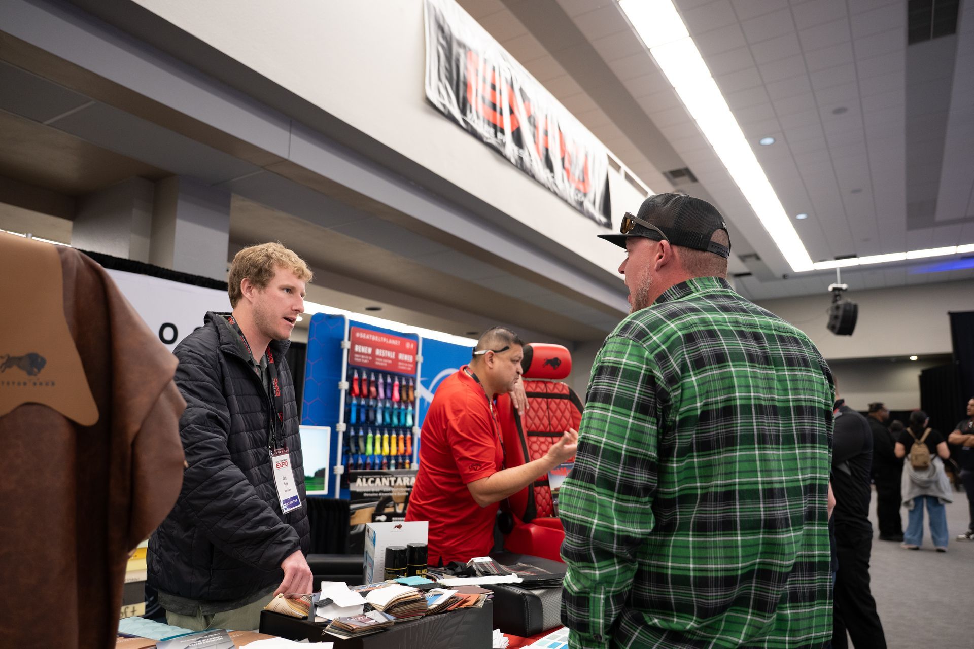 People interacting at a trade show booth, with product display and attendees in the background.