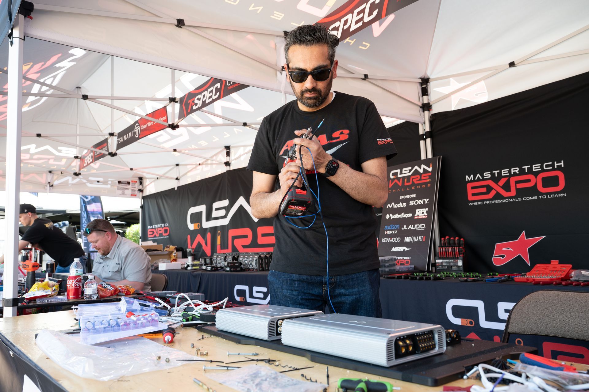 Man holding wires at a Clear Wire booth during the Listen Tech Expo. He's working on electronic equipment at a table.