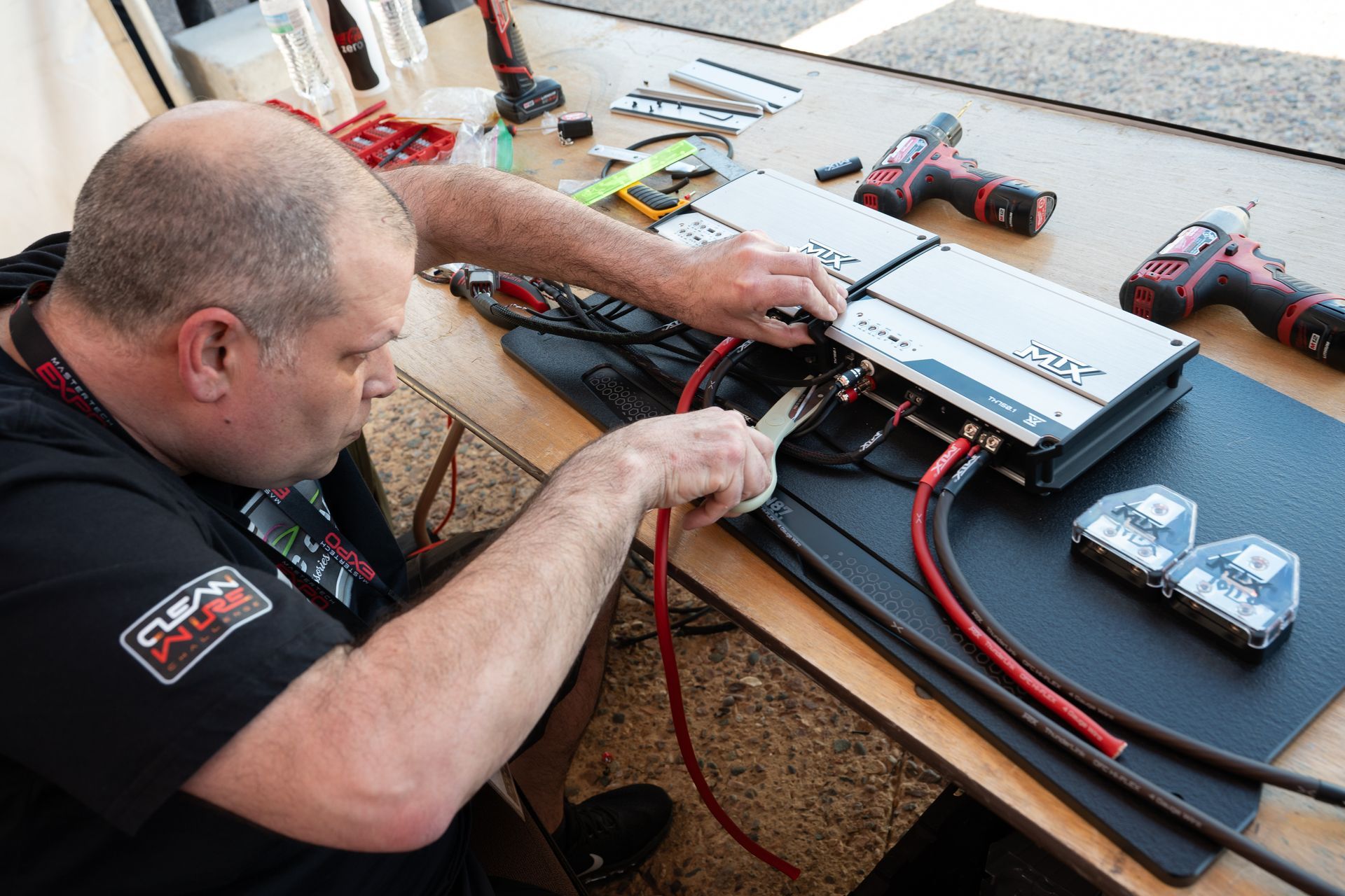 Man installing car audio amplifier, red cables, tools on table.