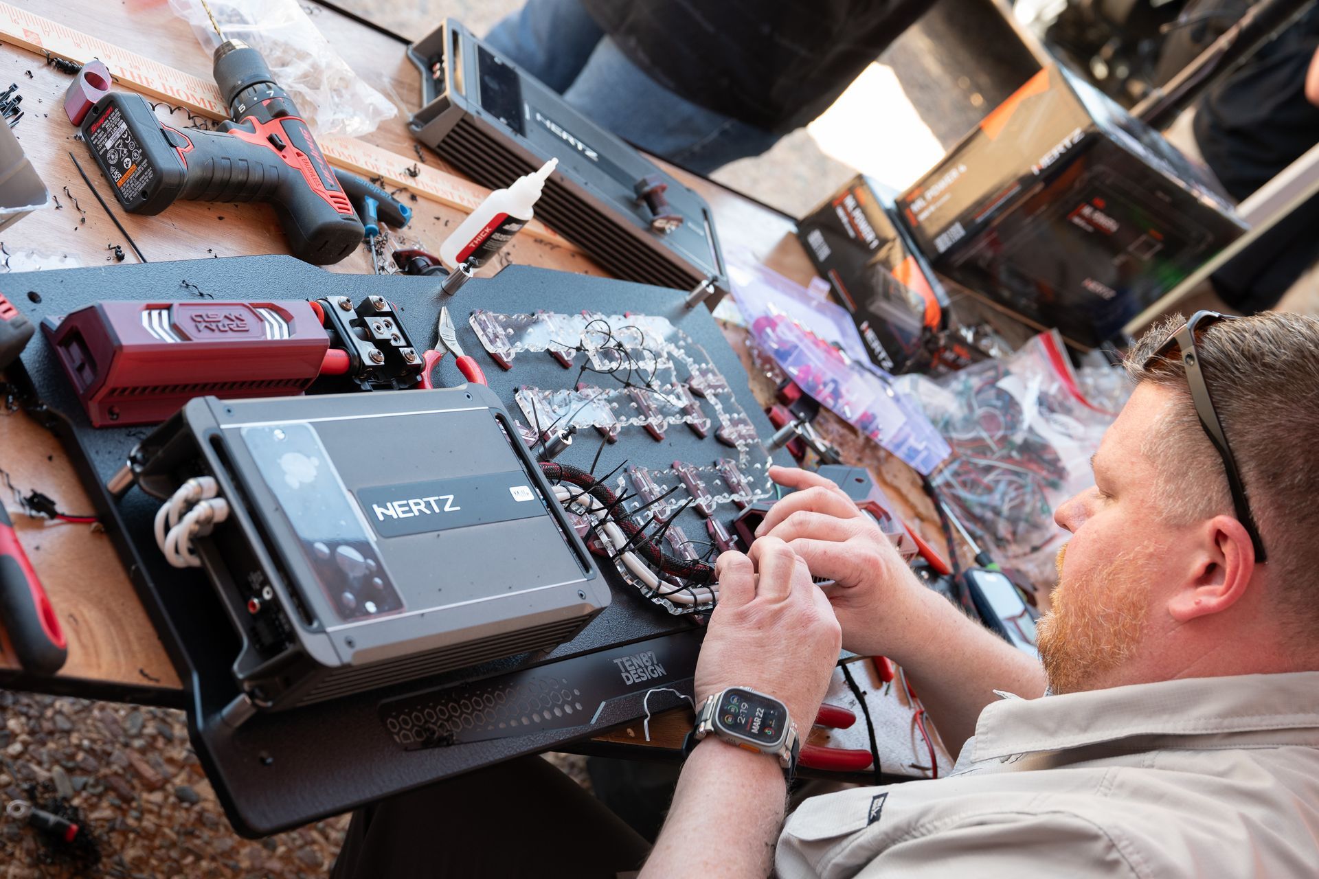 Man working on car audio components at a table with tools and equipment.