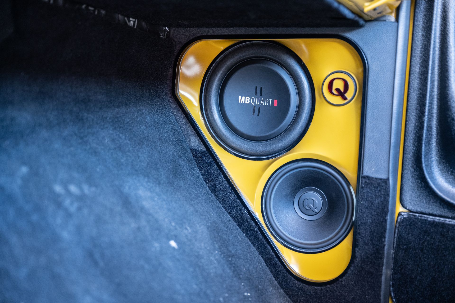 Yellow car audio speaker enclosure with two speakers on a black background.