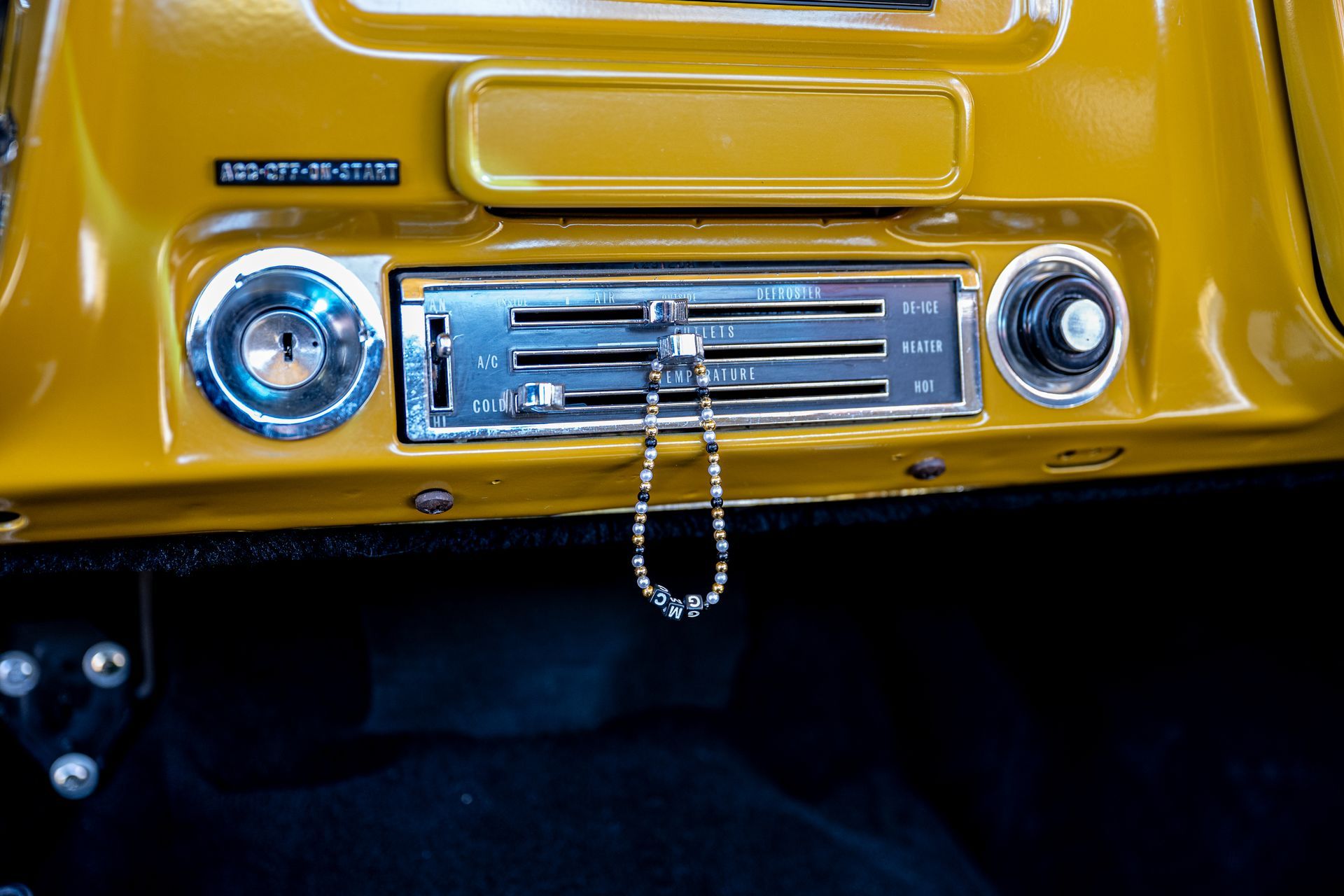 Yellow car dashboard with controls and a string of beads hanging from them.