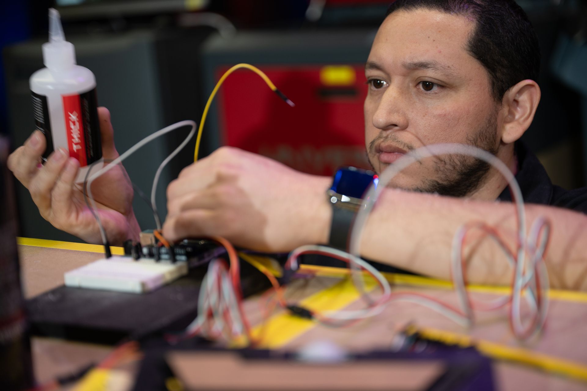 Man soldering wires onto a circuit board, holding glue bottle, focused, close-up.