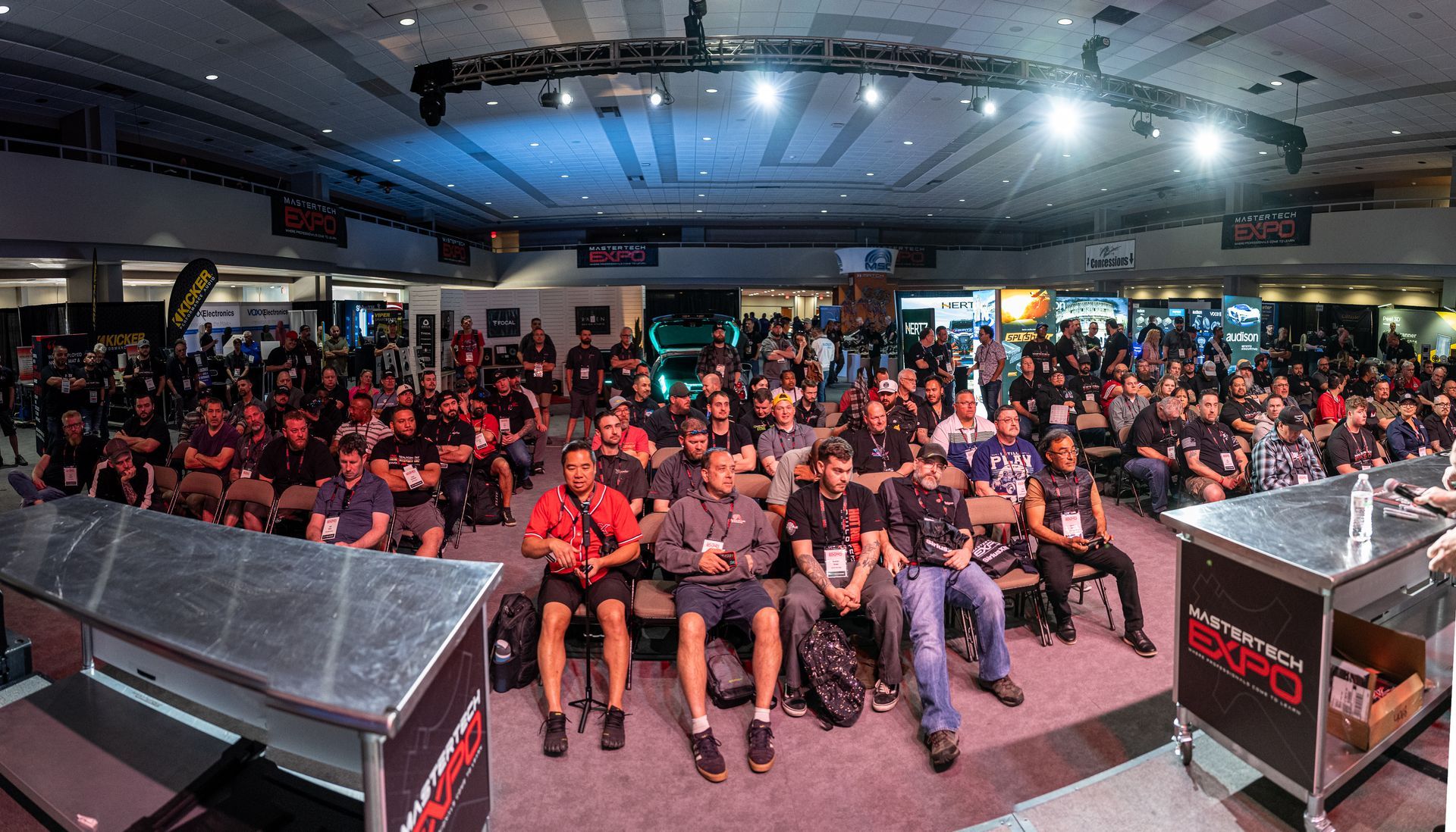 Large crowd in a conference hall watching a presentation; attendees seated, stage in front.