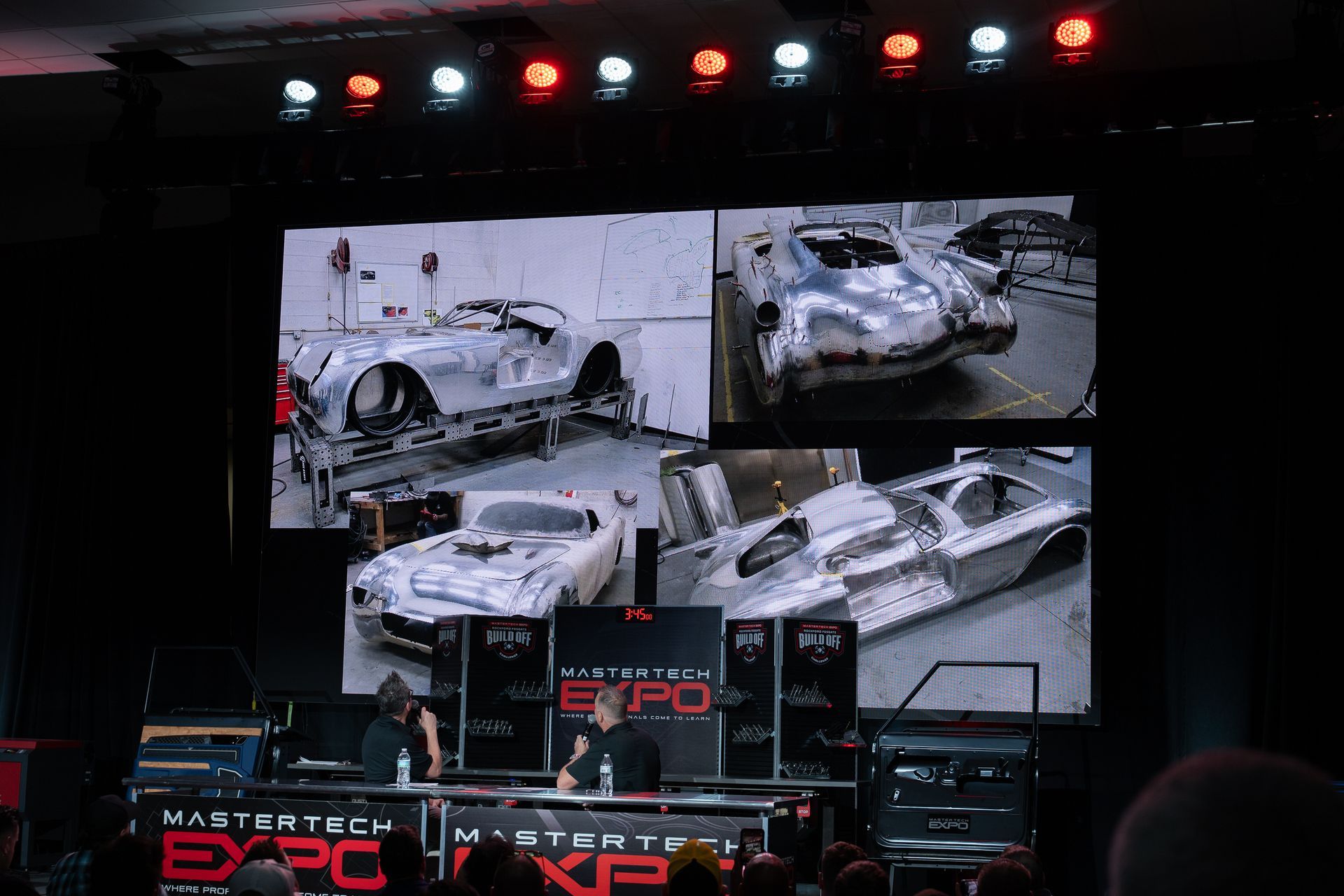 Two men on stage at Master Tech Expo, with car fabrication images displayed on a large screen.