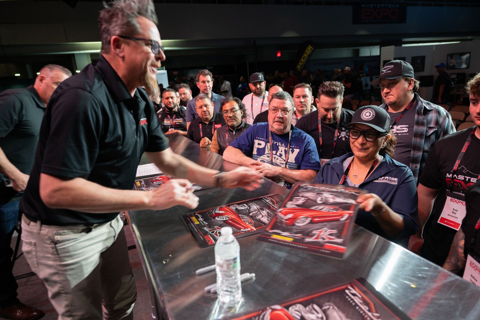 Man signing items for a woman, surrounded by a crowd at an event.