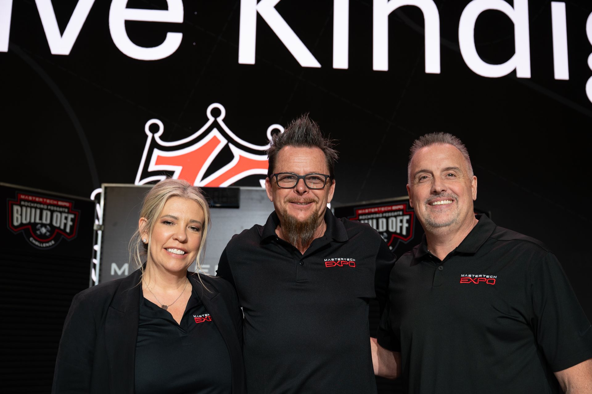 Three people in black shirts pose in front of a backdrop with a logo.