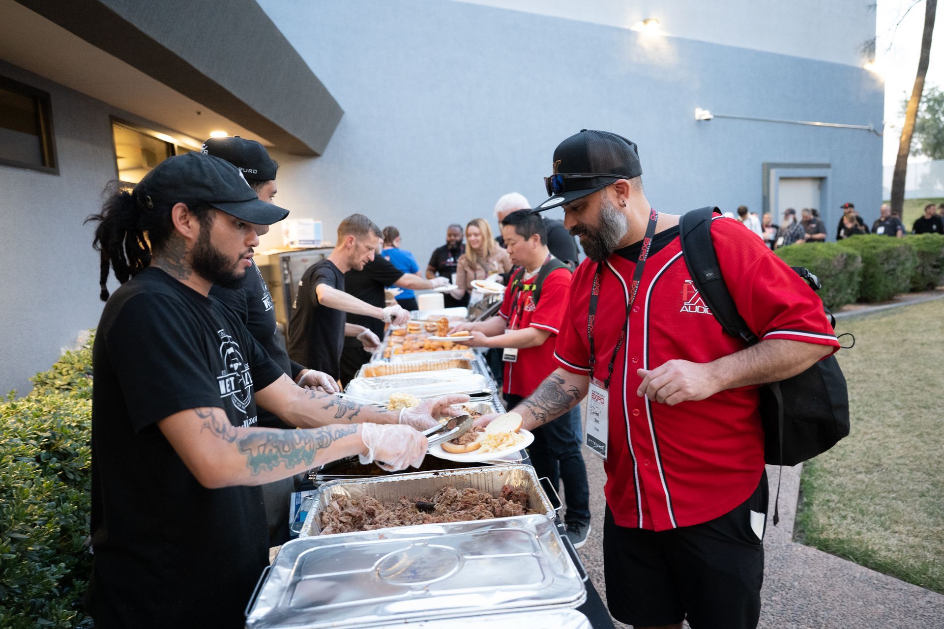People serving food at an outdoor buffet. Cooks with tattoos serve guests.