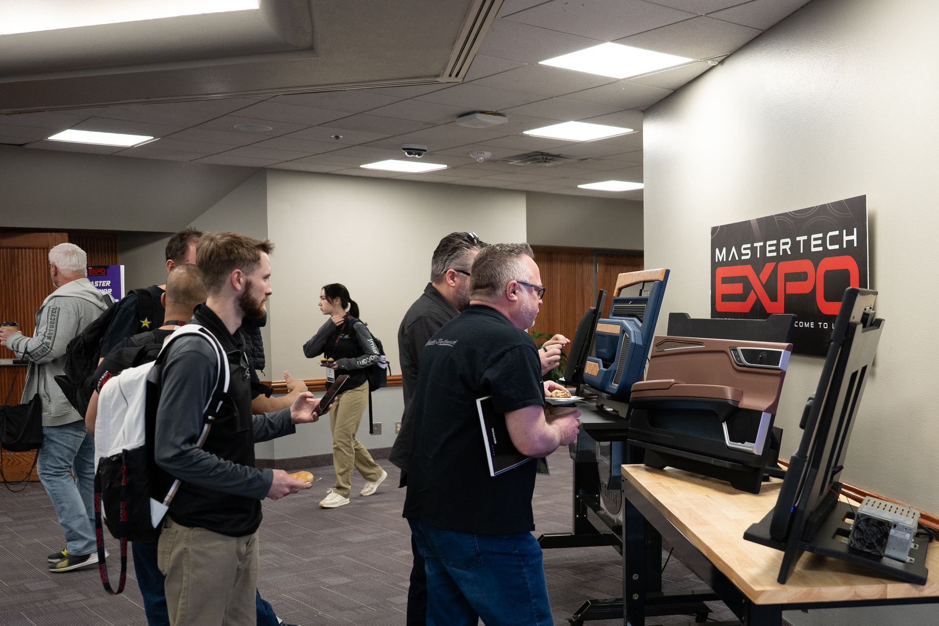 People at Mistertech Expo, looking at product displays. Interior, neutral tones, some holding items, logo visible.