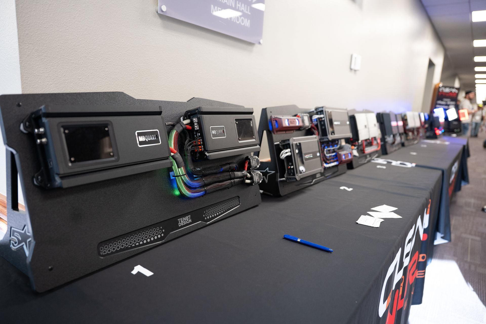 A row of black car audio amplifier displays on a table at an event.