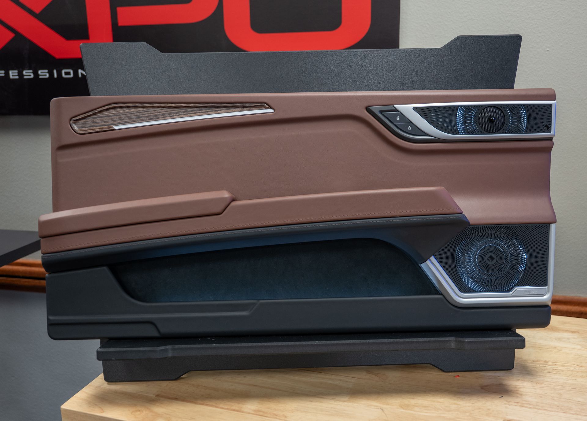 Brown and black car door panel with carbon fiber accents and speaker grill, on display.