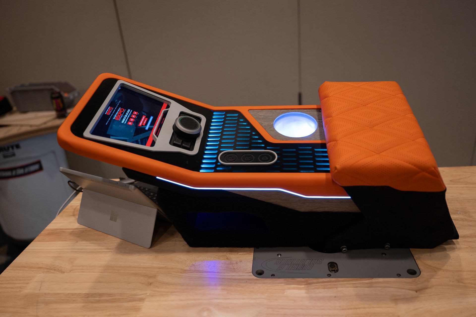 Orange and black custom console with a screen, buttons, and orange cushion, on a wooden table.