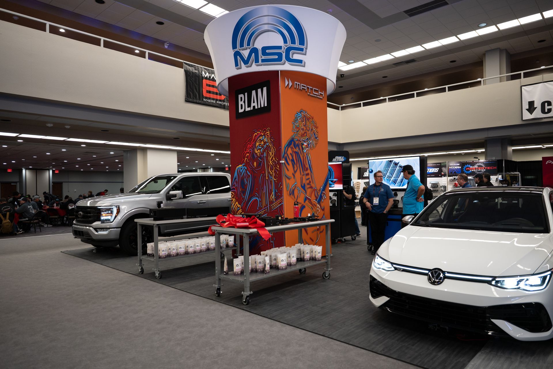 Convention hall with vehicles on display: a gray truck and a white car. Center column with MSC logo.