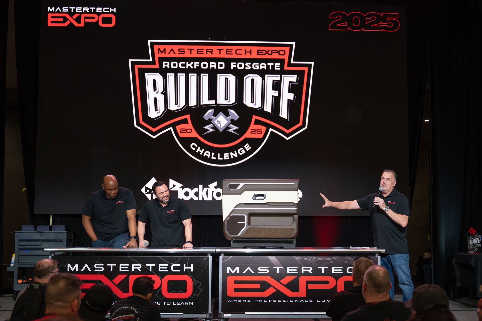 MasterTech Expo with Rockford Fosgate Build Off challenge. Men stand onstage, one speaks. Audience present.
