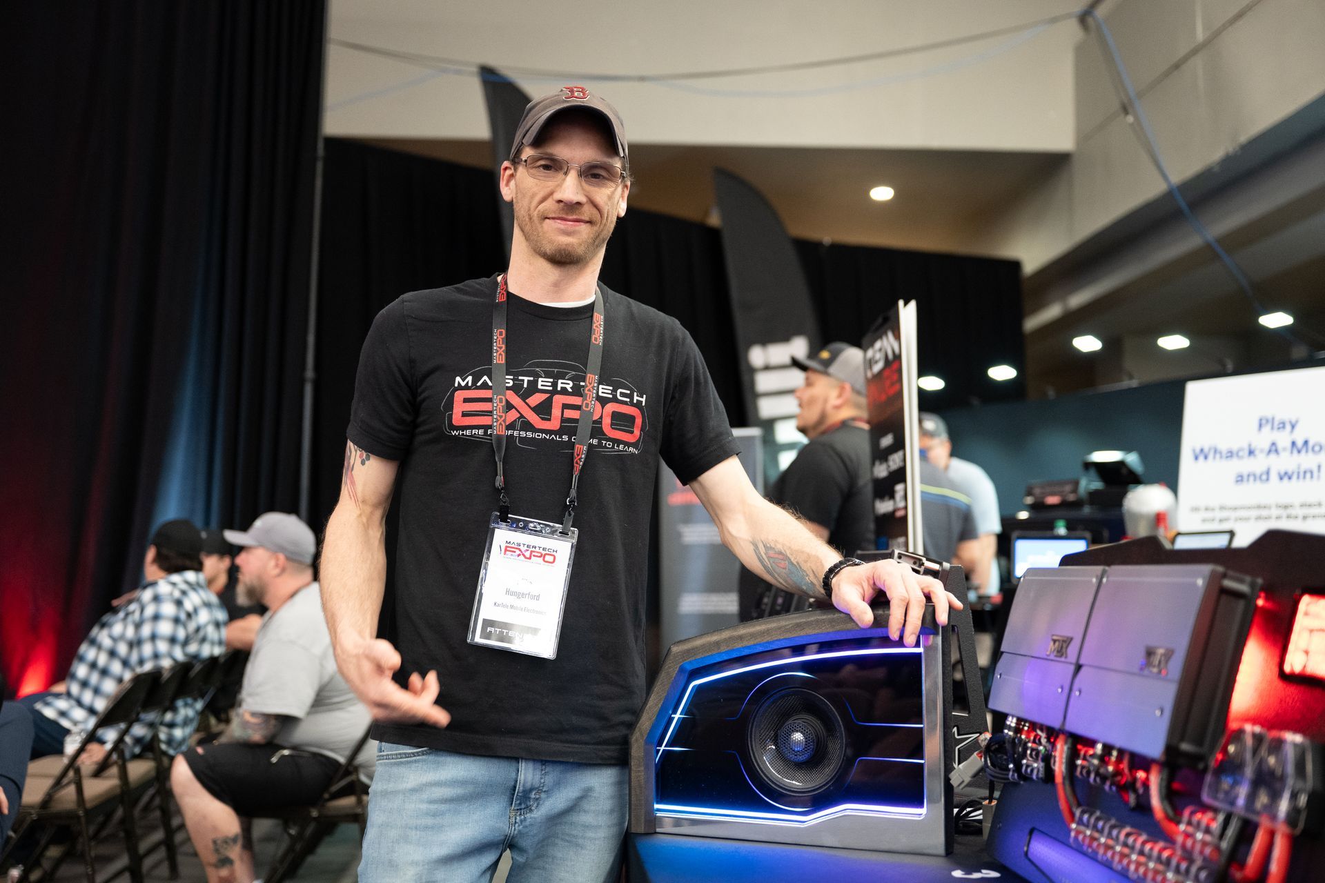 Man at an expo, pointing to car audio equipment with blue lights.