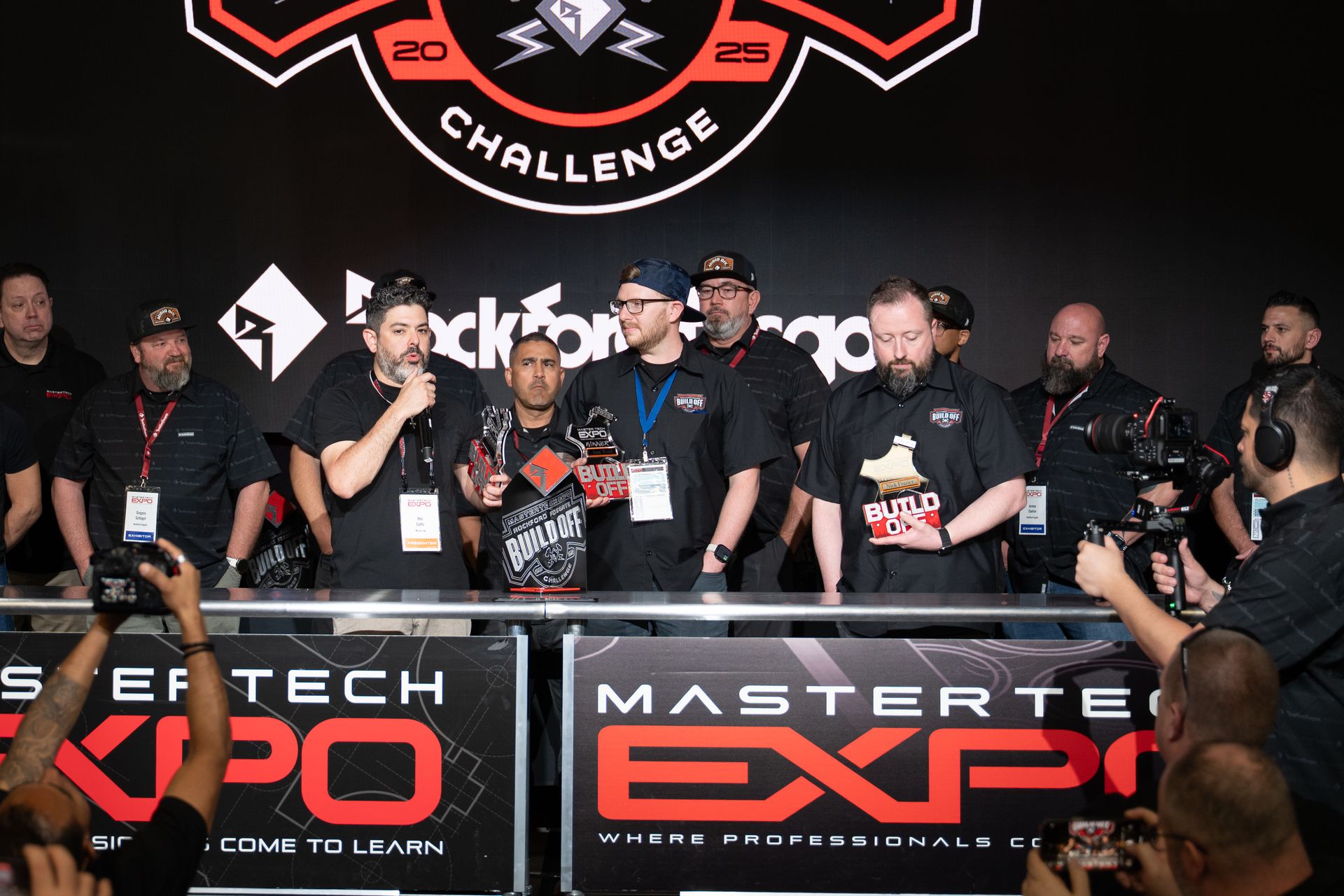 Group of men holding trophies on stage at the Mastertech Expo. They are celebrating a win.
