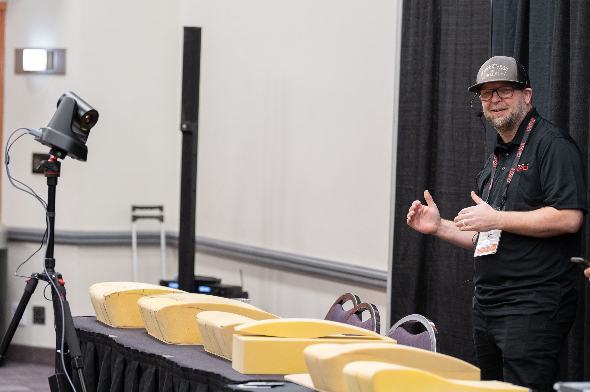 Man gesturing next to rows of foam blocks on a table, with a camera on a tripod.