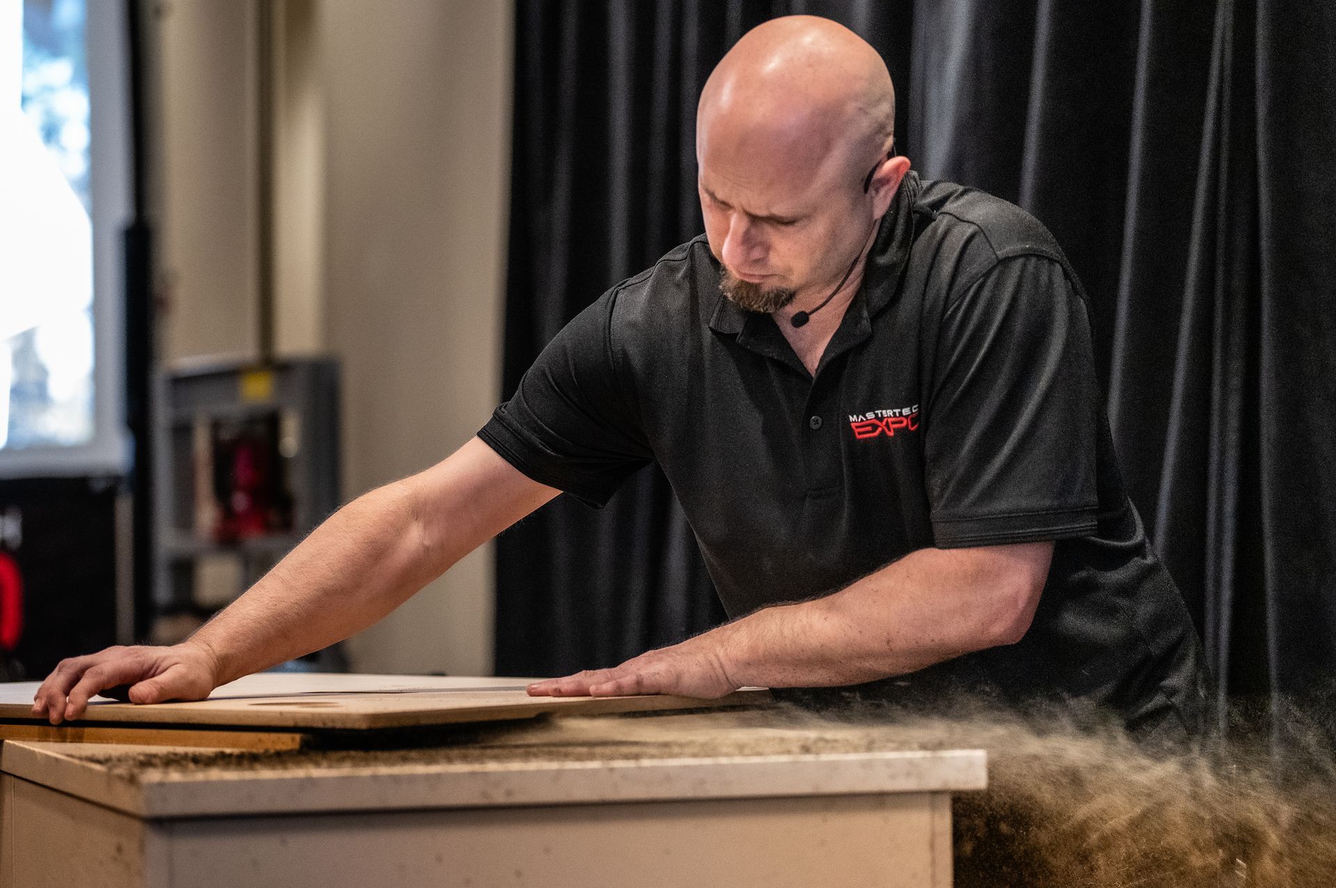 Man sanding wood, creating a cloud of sawdust.