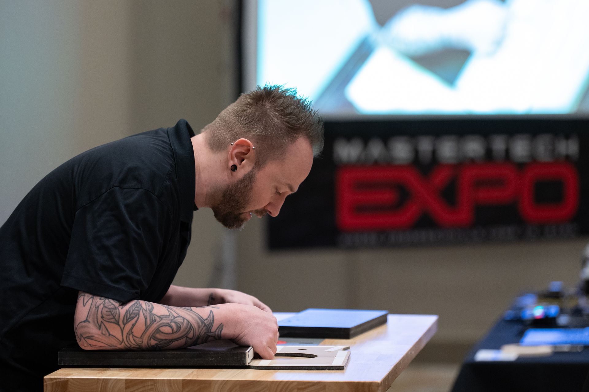 Man with tattoos at a table, looking down. 