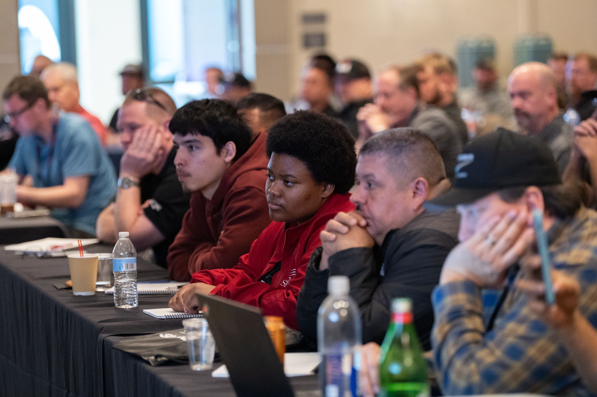 Attendees listening intently at a conference; some with hands on chins.