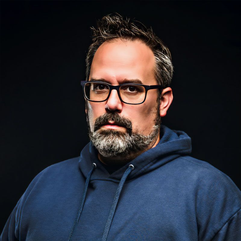 A man with a beard wearing glasses and a blue hoodie