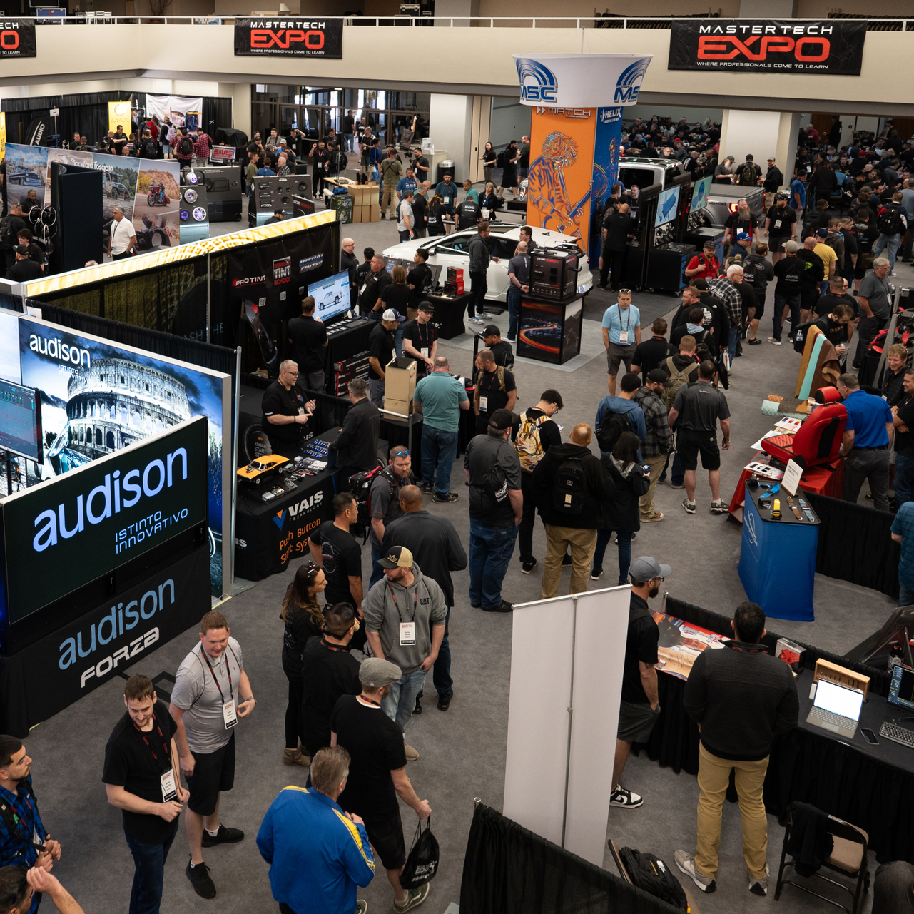 Large convention hall, people at booths, attending an expo.  Audison logo prominent.
