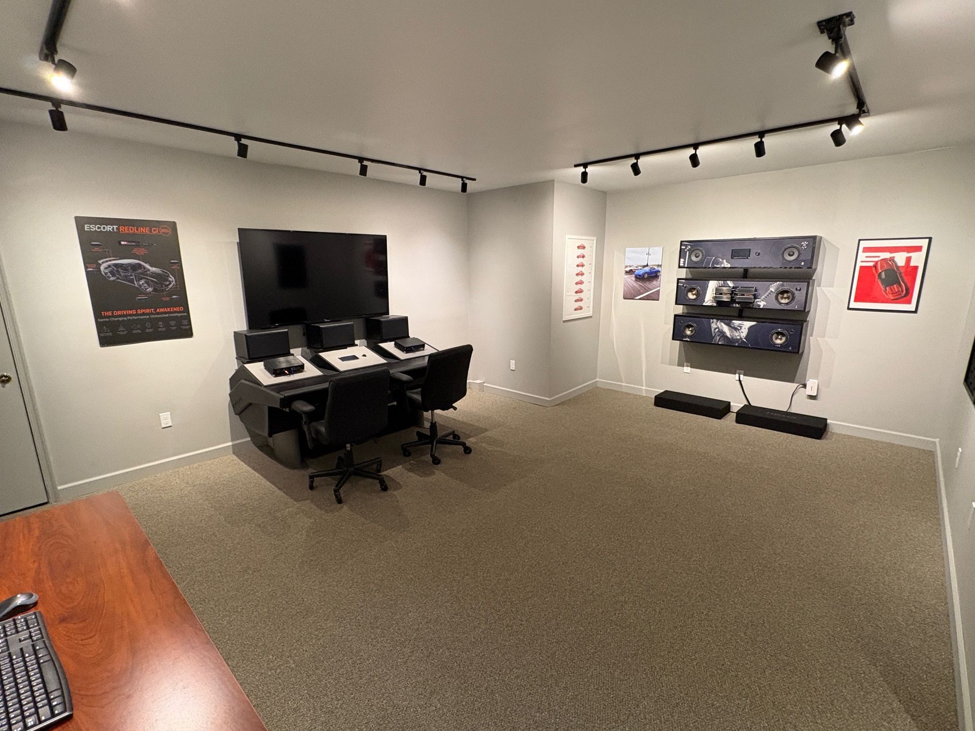 A home office with multiple computer setups, black furniture, and framed artwork on the walls.