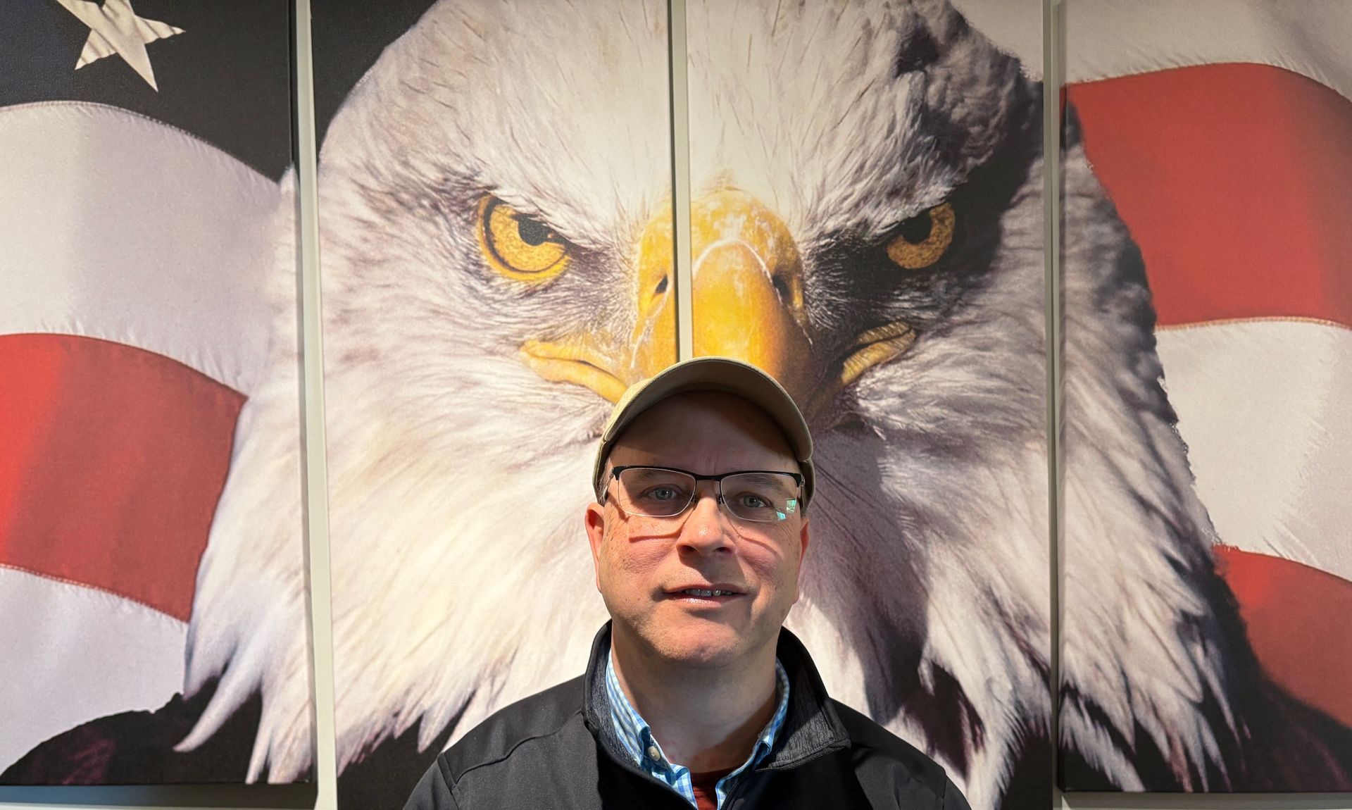 A man is standing in front of a bald eagle and an american flag.