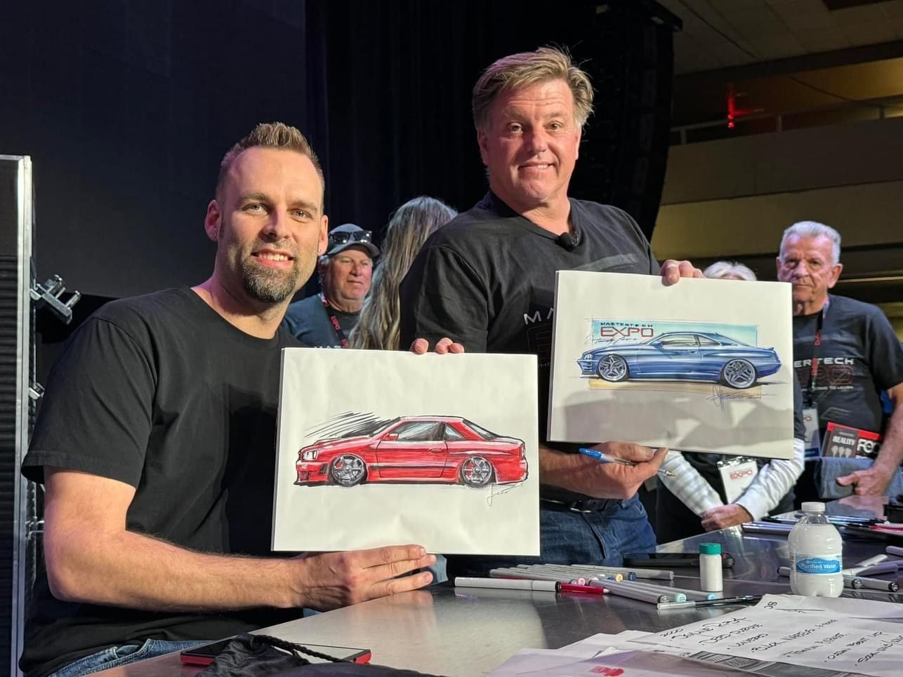 Two men are holding drawings of cars in their hands.