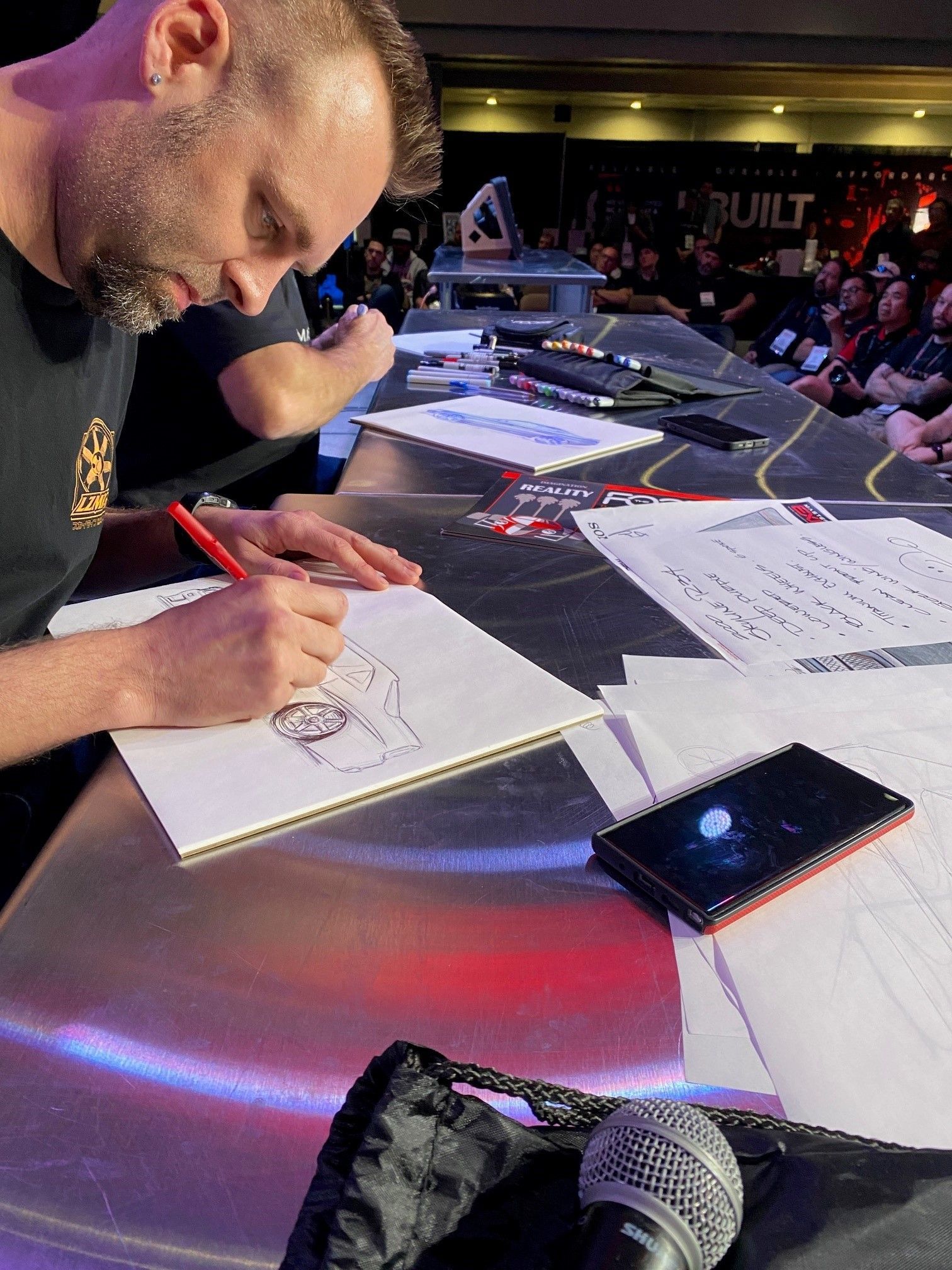 A man is sitting at a table drawing on a piece of paper.