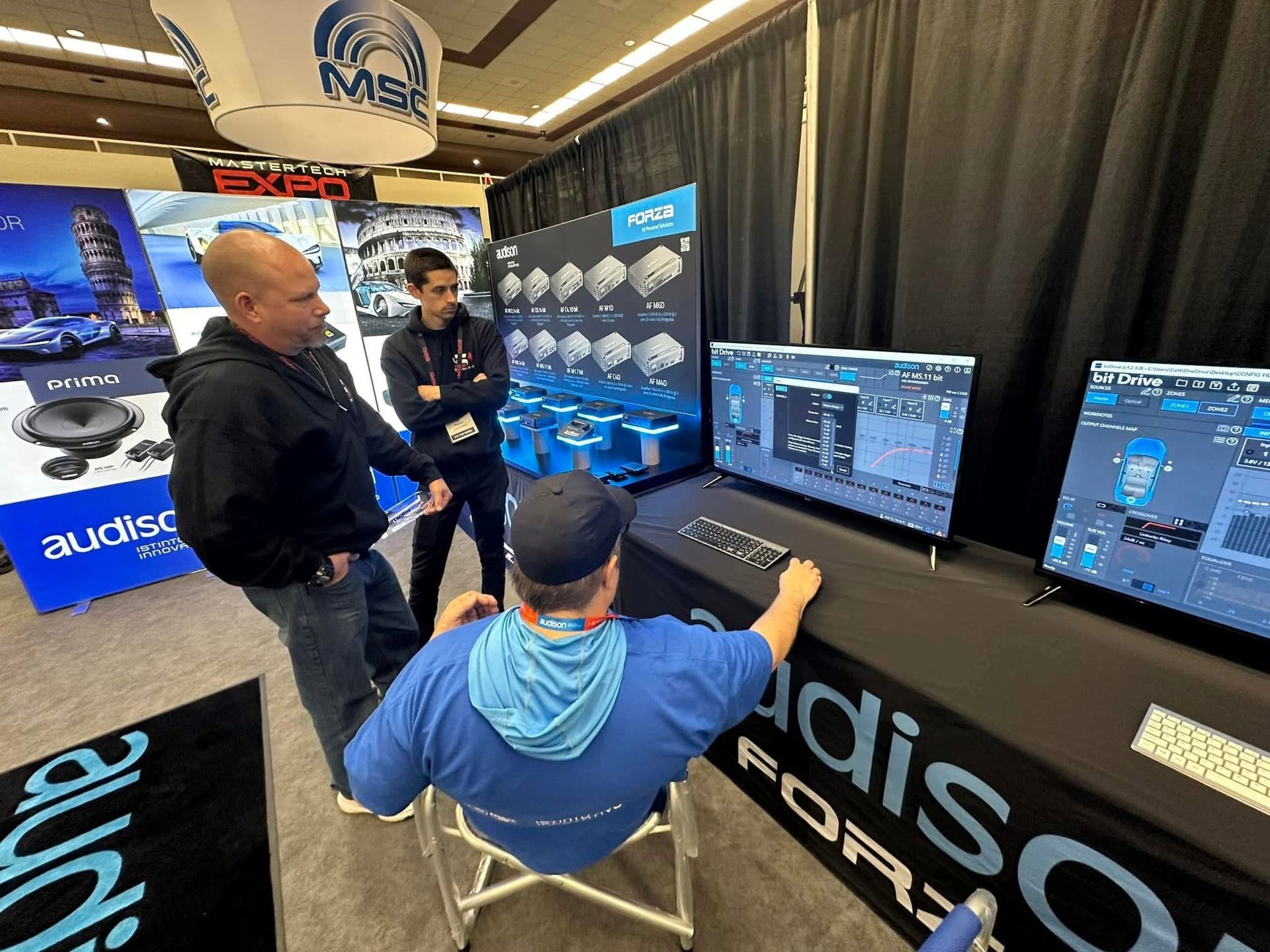 A man is sitting at a table in front of a computer monitor.