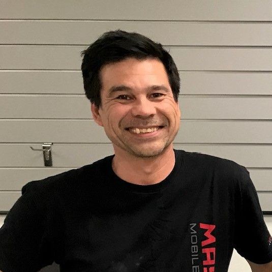 A man wearing a black t-shirt with the word mobile on it is smiling.