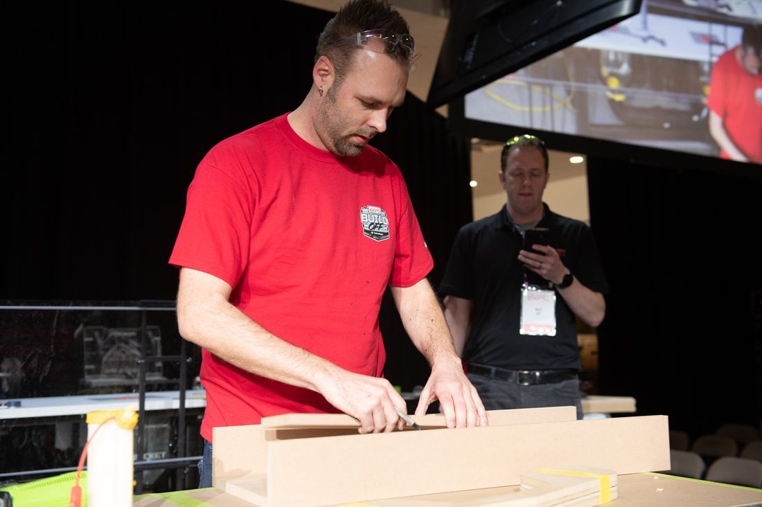 A man in a red shirt is working on a piece of cardboard.