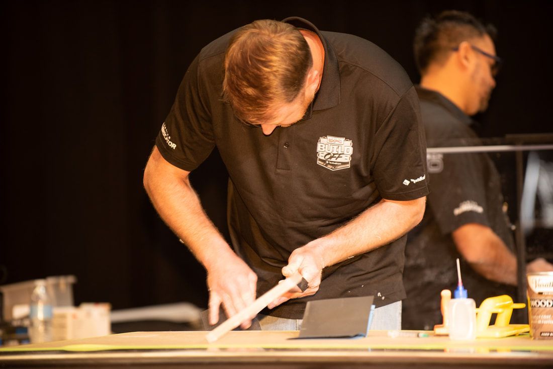 A man in a black shirt is working on a piece of wood.